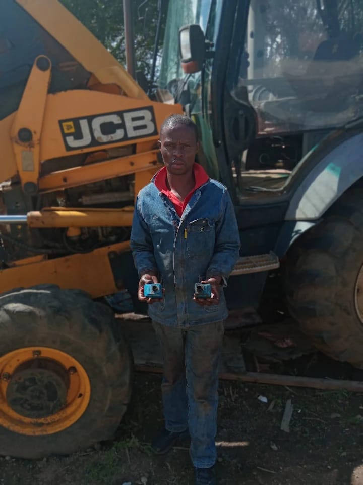 Technician holding rebuilt hydraulic components beside a JCB TLB